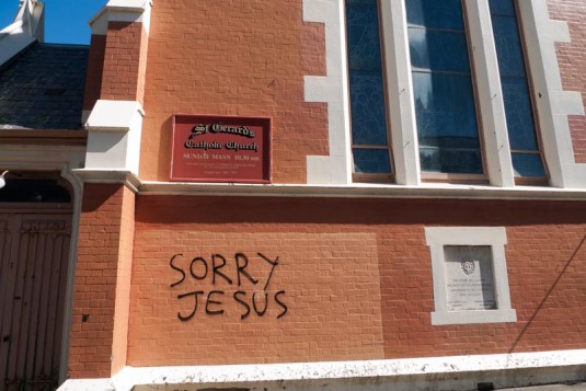 The brick wall of St Gerrard's Catholic Church in Hawker Street, with graffiti saying "SORRY JESUS"