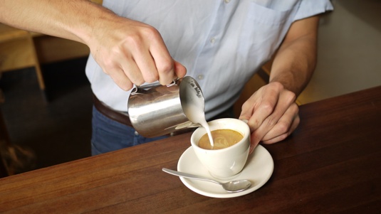 Image of Richard Legg's hands pouring milk into a coffee.
