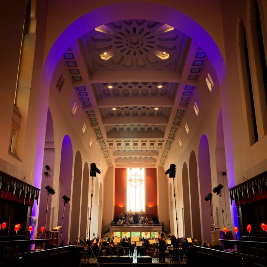 Interior of St. Pauls, looking down the nave toward the rear window. The orchestra's chairs and stands are empty as the audience waits for the concert to begin.