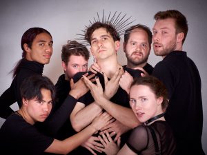 The cast of The Slutcracker surround Jake Brown who is wearing a star-like crown and posing with hands crossed in front of him. They are all looking out at the viewer. 