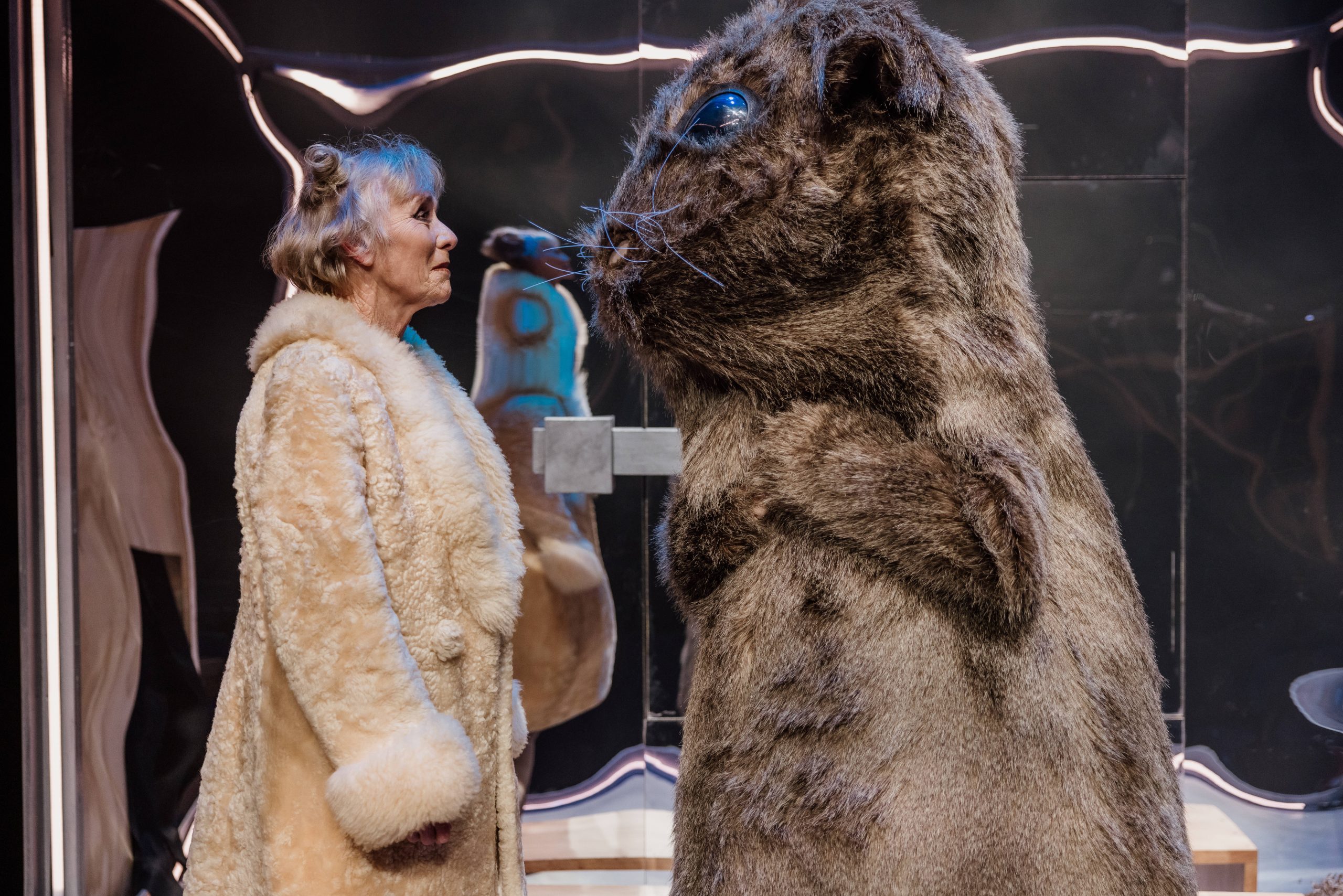 Actress dressed in furcoat looks into the eyes of a human sized guinea pig