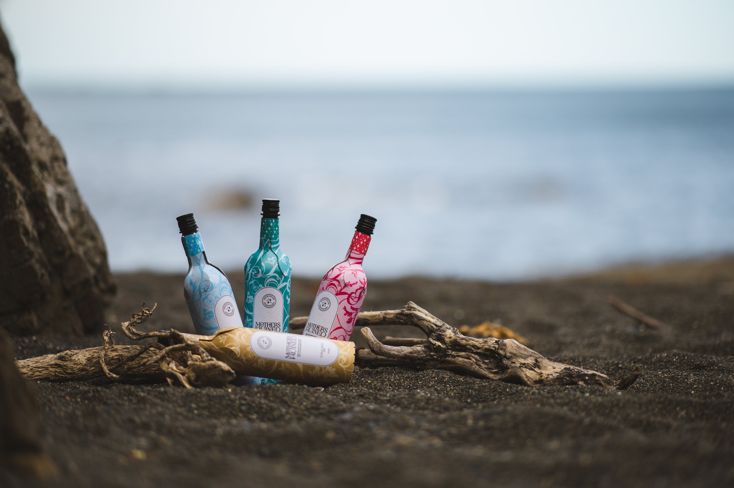 paper bottles of Mothers Ruined Gin on a beach